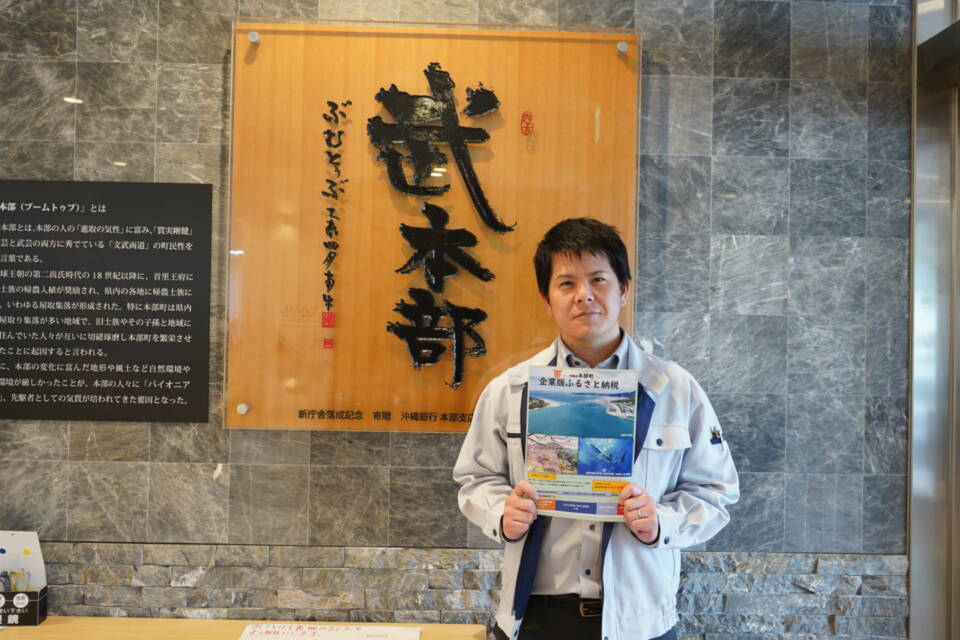 本部町民の質実剛健かつ文武両道の気質を表す「武本部」の文字の前に立つ、玉城将吾さん